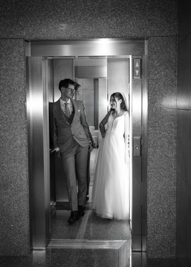 Fotografia ślubna Grudziądz – nowoczesny reportaż ślubny z Hotelu Rudnik. Czarno-białe zdjęcie pary młodej pozującej w metalowej windzie hotelowej; panna młoda w klasycznej sukni ślubnej i pan młody w garniturze patrzą na siebie z uśmiechem.