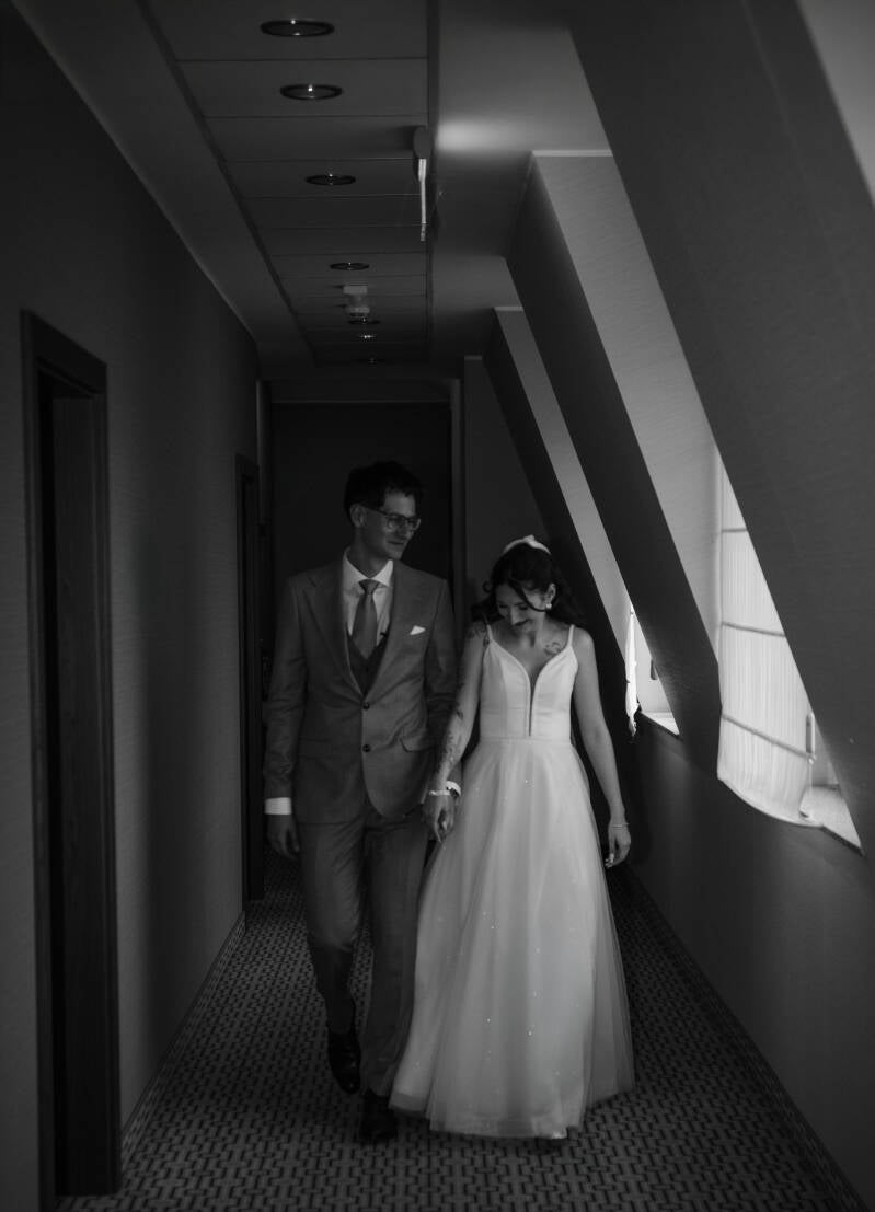 Fotograf ślubny Grudziądz i okolice – nowoczesna sesja ślubna blisko Chełmna oraz Świecia. Para młoda idzie korytarzem hotelowym w stronę błogosławieństwa od rodziców, prezentując eleganckie stroje weselne.