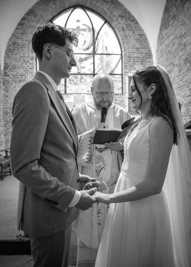Fotografia ślubna Grudziądz – przysięga małżeńska Wiktorii i Dawida w kościele w Piaskach. Czarno-biały, bliski kadr przedstawiający parę młodą trzymającą się za dłonie przed ołtarzem i składającą przysięgę w obecności księdza.