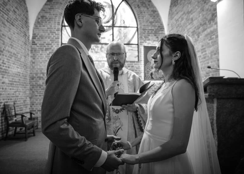 Fotograf ślubny Grudziądz i okolice – wzruszający reportaż ślubny z ceremonii blisko Torunia i Bydgoszczy. Nowożeńcy patrzą na siebie z miłością podczas ślubowania, w tle widoczne jest zabytkowe, ceglane wnętrze świątyni z dużym oknem witrażowym.