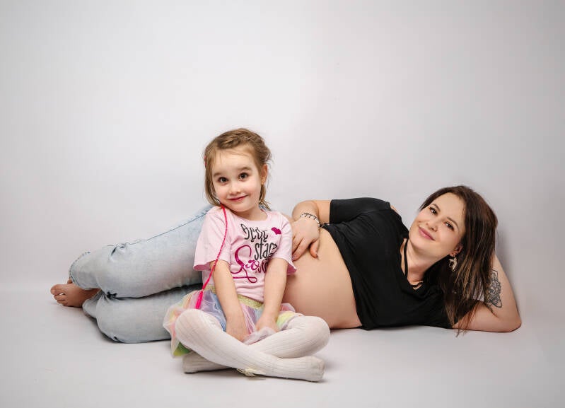 Mała dziewczynka w różowej koszulce „Będę starszą siostrą” i jej mama na wspólnej sesji brzuszkowej w województwie kujawsko-pomorskim