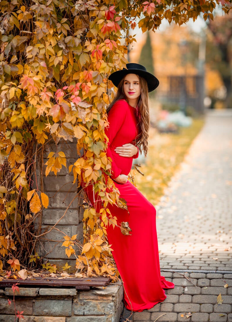 Przyszła mama w długiej czerwonej sukni eksponującej ciążowy brzuszek pozuje w grudziądzkim Ogrodzie Botanicznym – fotografka ciążowa Grudziądz