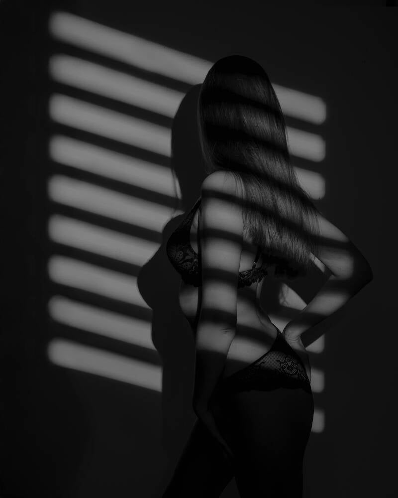 Sesja kobieca Grudziądz – fotografia sensualna i buduarowa w studio. Czarno-biały portret kobiety w koronkowej bieliźnie, na którą padają geometryczne pasy światła z żaluzji