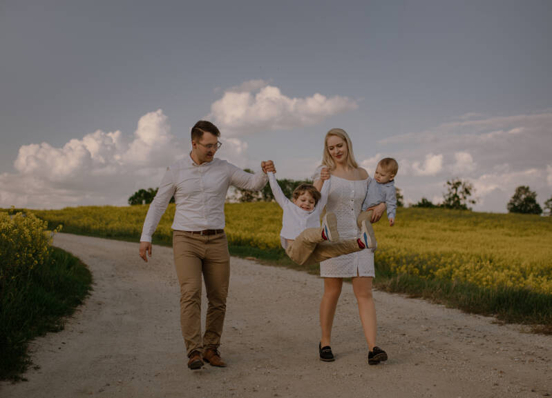 Mama, tata i dwójka dzieci podczas spaceru wiejską drogą obok pola rzepaku – plenerowa sesja rodzinna i roczkowa w okolicach Grudziądza