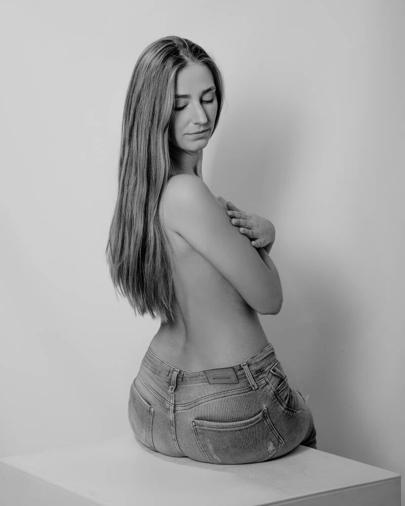 Czarno-białe ujęcie topless kobiety od tyłu w dopasowanych jeansach, siedzącej na kostce z przymkniętymi oczami – artystyczna sesja kobieca w Grudziądzu