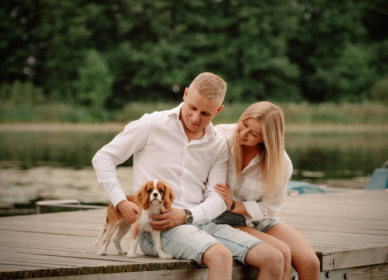 Partnerska sesja zdjęciowa z pupilem nad jeziorem w luźnych, letnich stylizacjach – fotografia rodzinna dla klientów z okolic Torunia i Bydgoszczy