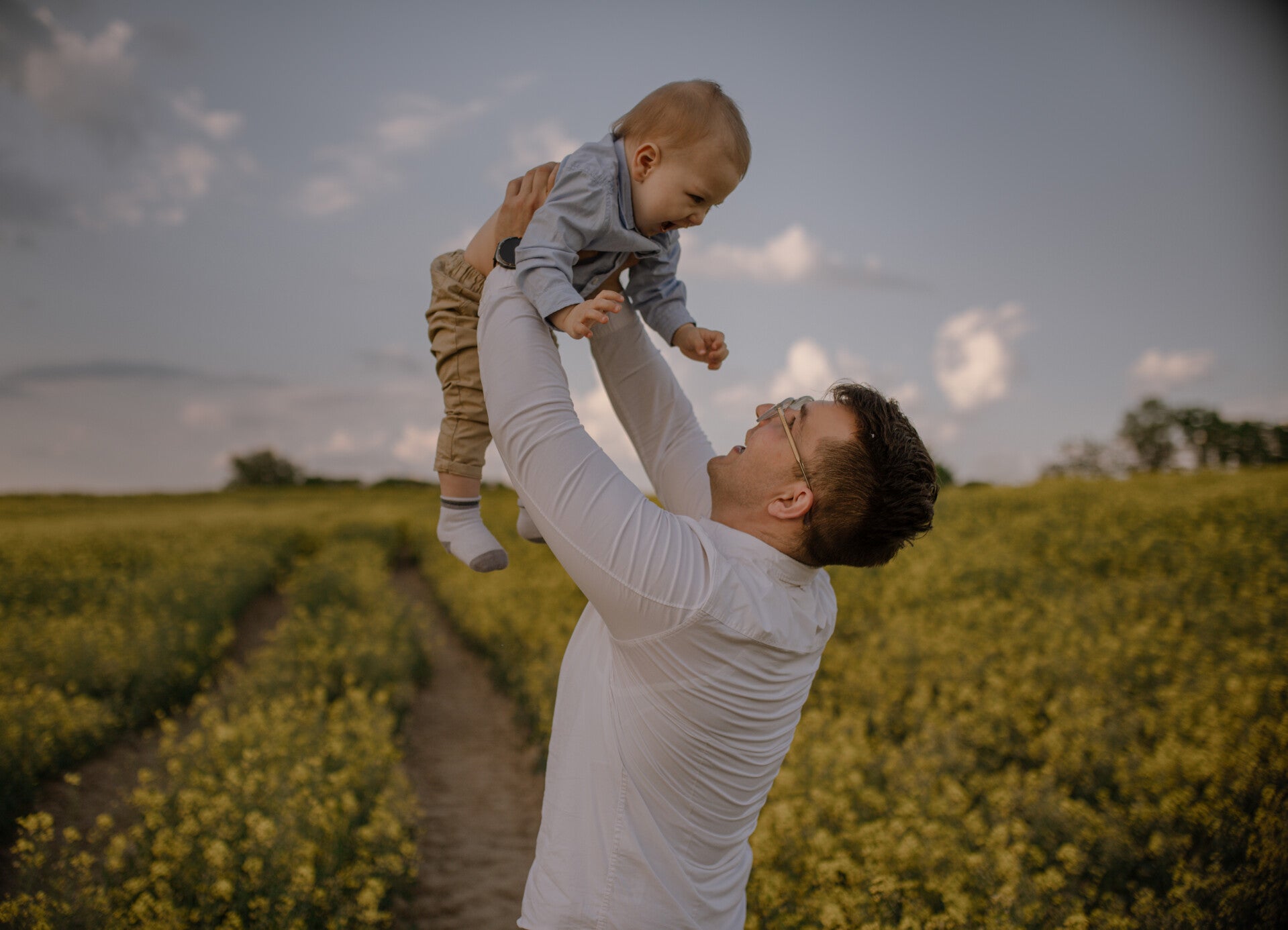  Marcin podrzuca małego Frania podczas rodzinnych zdjęć plenerowych w rzepaku – fotograf dziecięcy blisko Torunia i Bydgoszczy