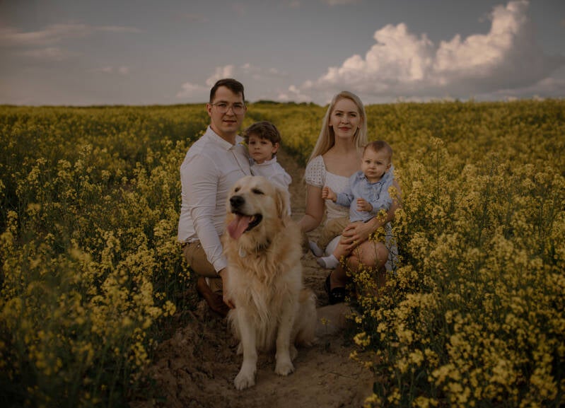 Portret rodzinny na polu rzepaku – mama, tata, dwójka dzieci oraz uśmiechnięty pies golden retriever podczas sesji w okolicach Grudziądza