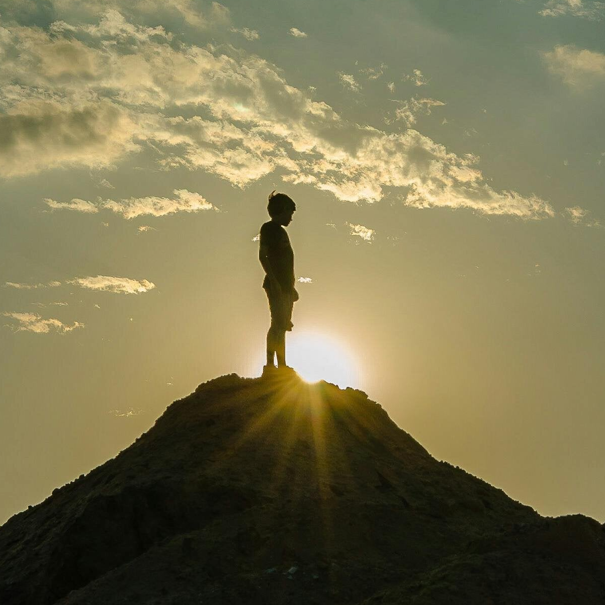 auf einem Berggipfel stehende Person mit Sonnen die dahinter aufgeht