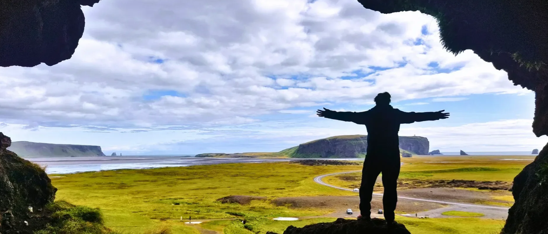 Iemand met open armen in een grot die uitkijkt over een ijslands landschap