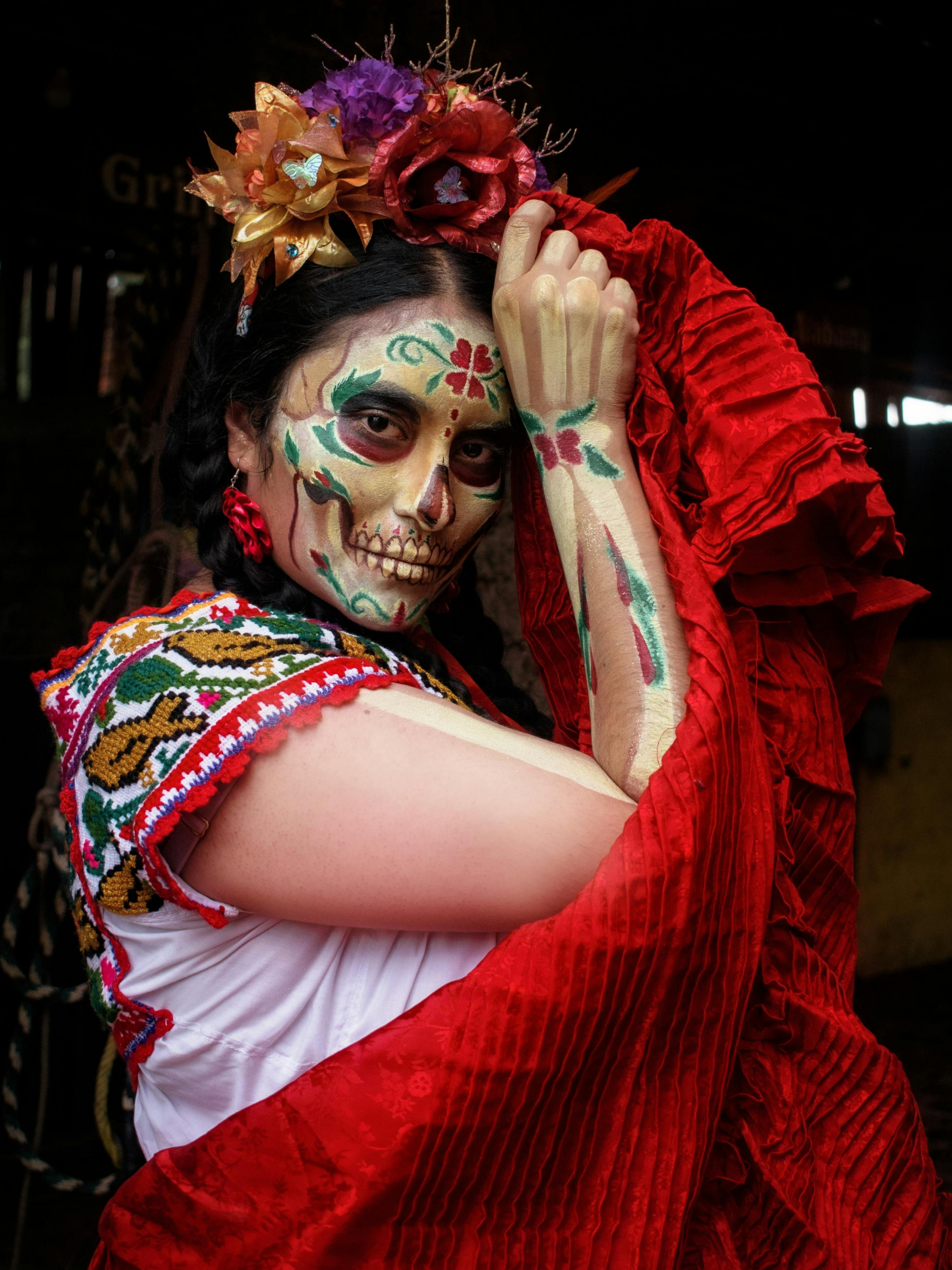 Vrouw met een schedel geschilderd op haar gezicht kijkt in de lens. Het is een portret tijdens Día de los Muertos in Mexico