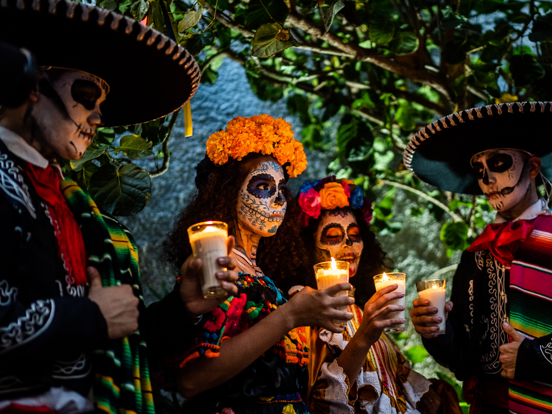 4 mensen hebben kaarsen vast, hun gezichten zijn geschilderd als schedel. Tijdens Día de los Muertos herdenken ze de doden in Mexico