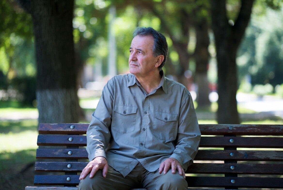 Thoughtful man in his 60s sitting on a park bench, representing the wisdom and experience AI cannot replace