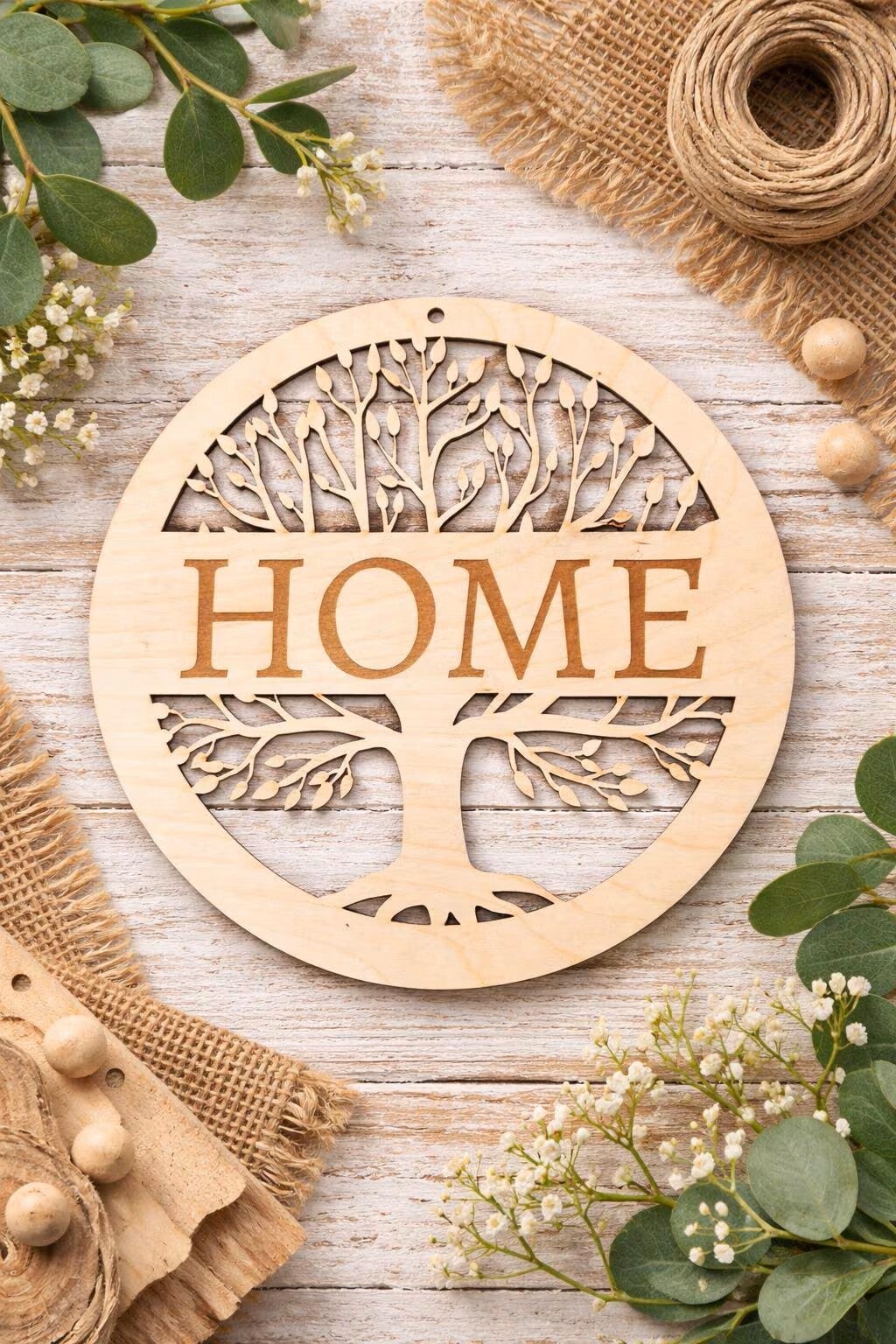 Rundes Holzschild mit Lebensbaum-Motiv und Schriftzug "HOME", dekoriert mit Eukalyptus