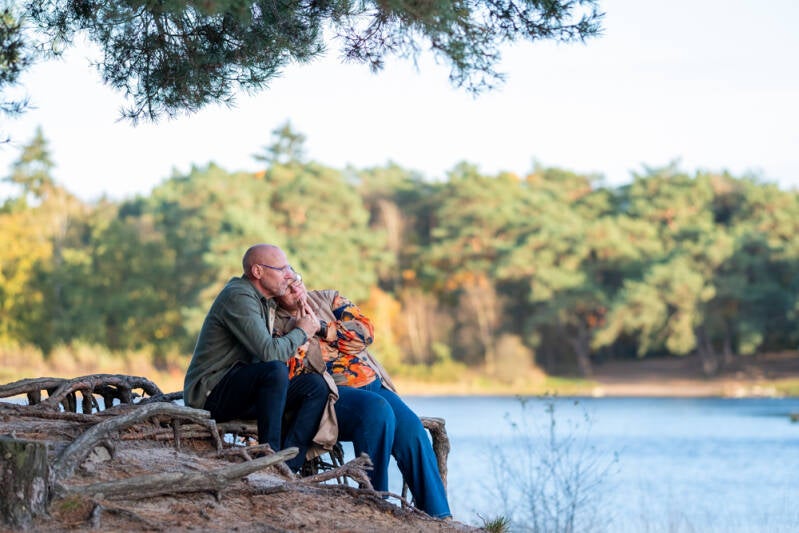 Liefdevol koppel in innige omhelzing, zittend op de wortels van een boom aan een ven.