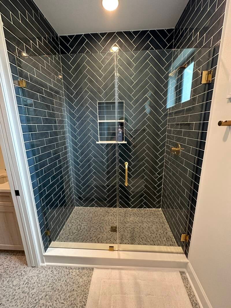 Custom walk-in shower with dark herringbone tile, frameless glass and brushed gold fixtures in Monmouth County NJ