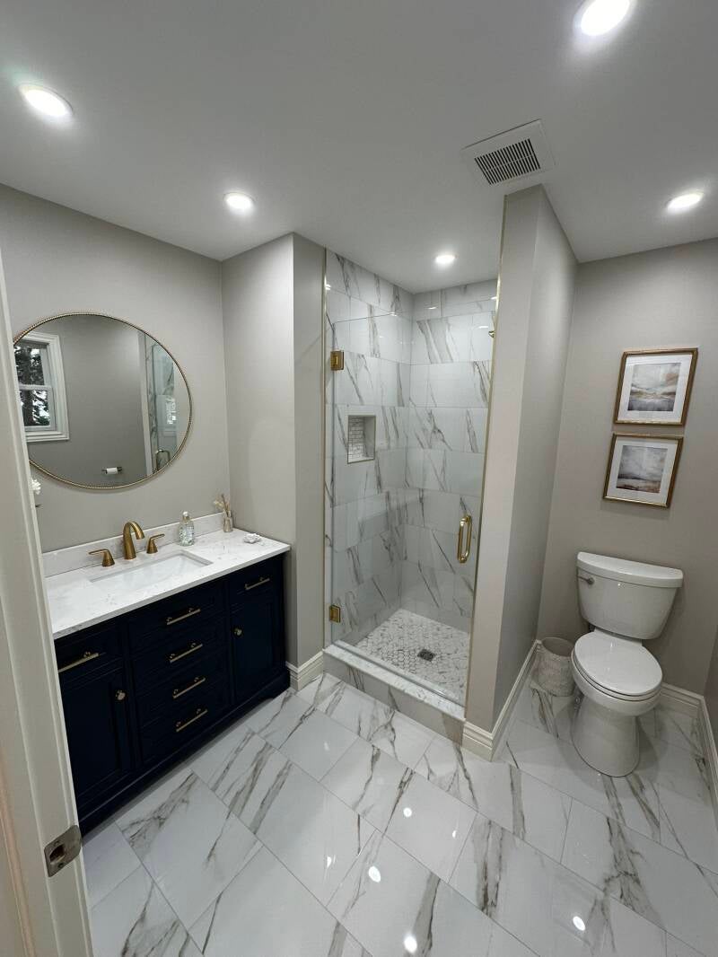 Bathroom remodel with navy vanity, marble-look tile and brushed gold fixtures in Monmouth County NJ
