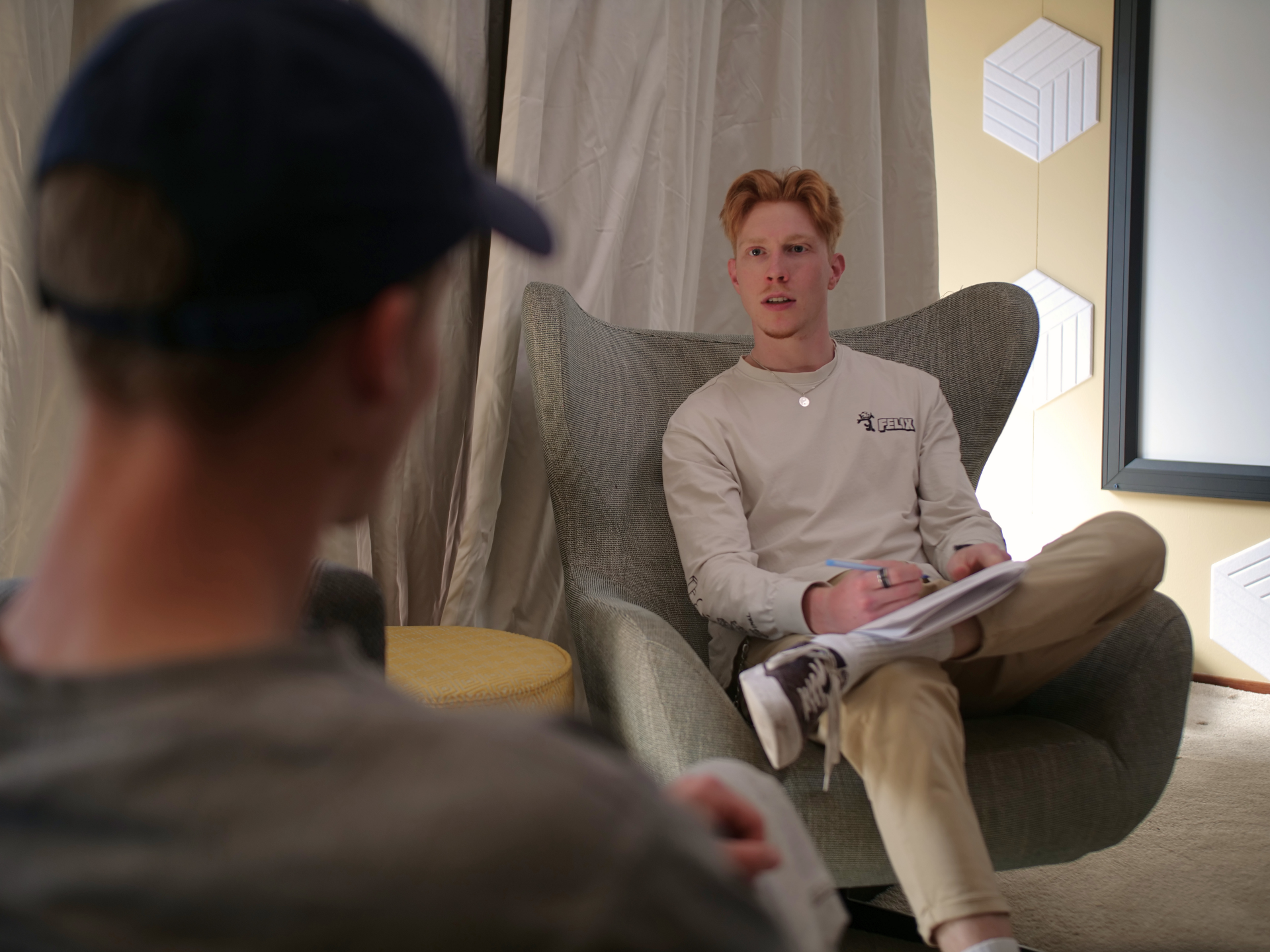 Student met rood haar zit in een moderne stoel en kijkt luisterend naar zijn gesprekspartner.