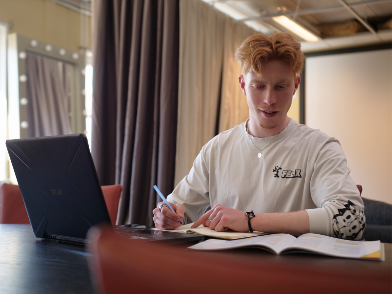 Studiekeuzebegeleider die het rapport van de kandidaat aan het bestuderen is aan een houten tafel met zijn laptop en het rapport voor zich.