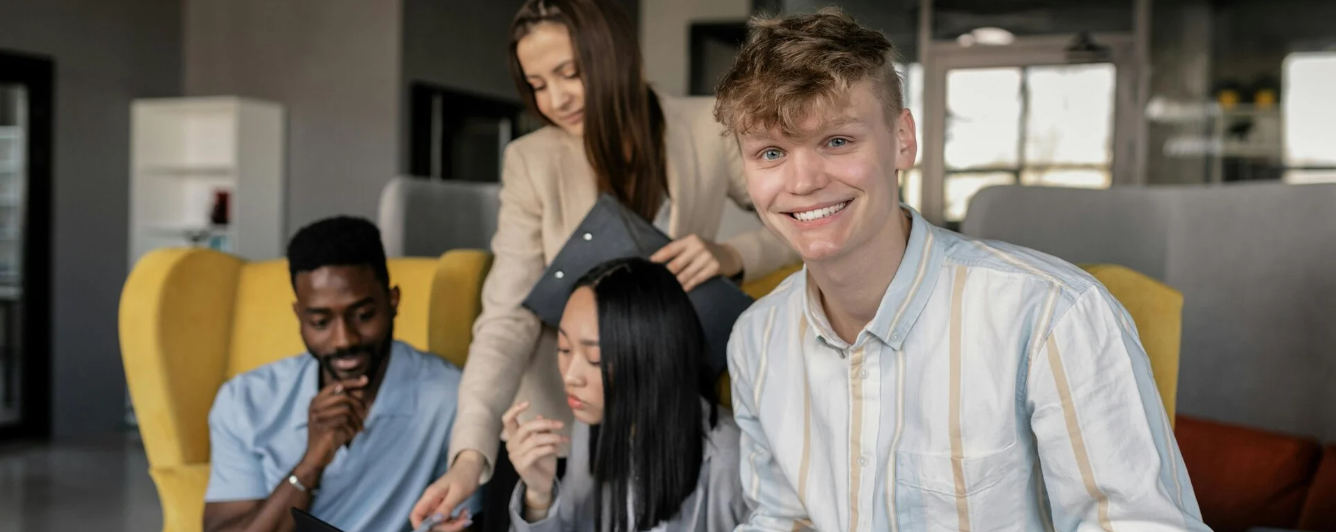 Vier studenten die in een openbare ruimte van de school zitten te studeren in relaxte stoelen, waarvan één lachend naar de camera kijkt.