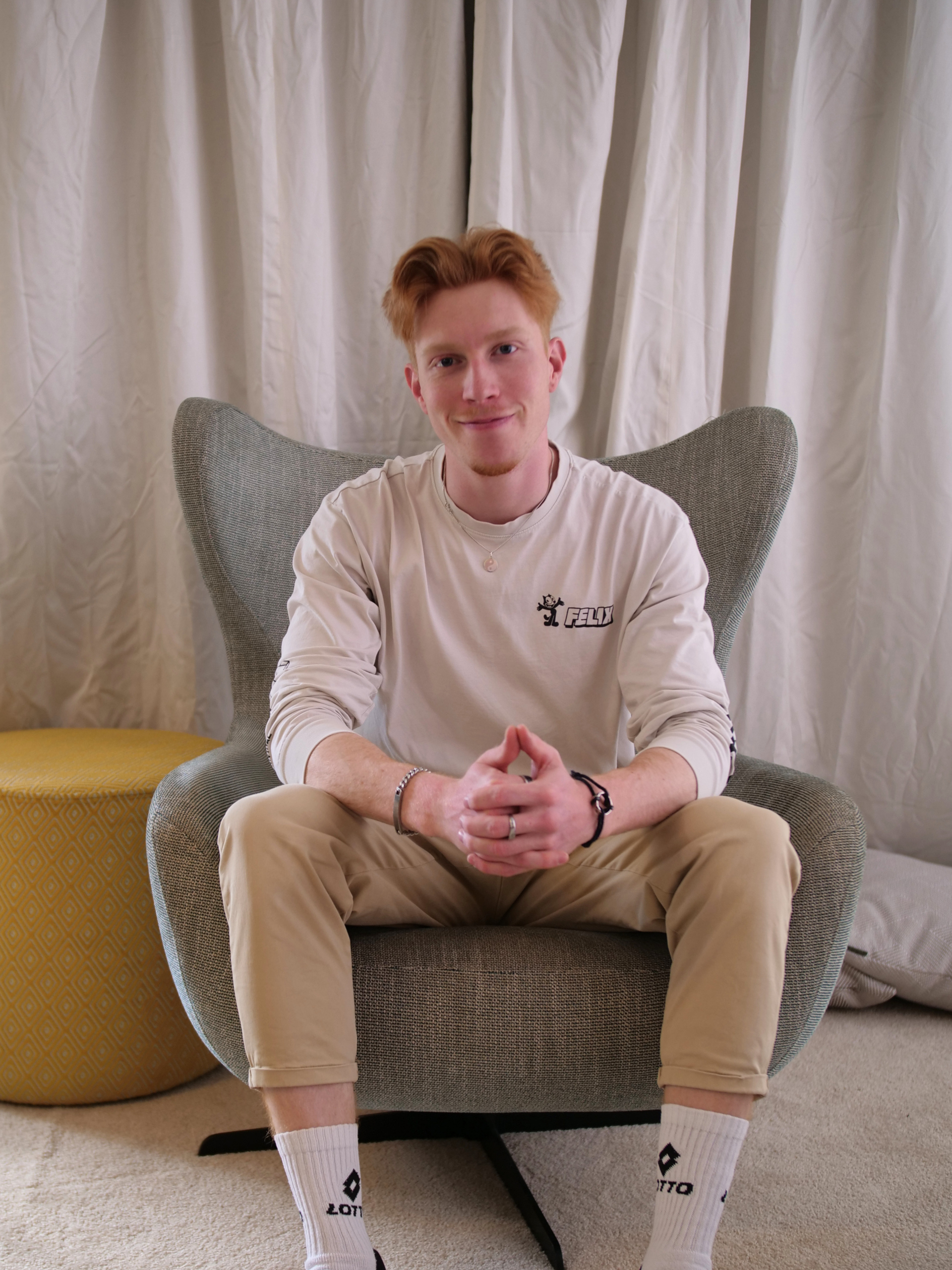 Portret van een glimlachende student die ontspannen in een stoel zit met gevouwen handen.