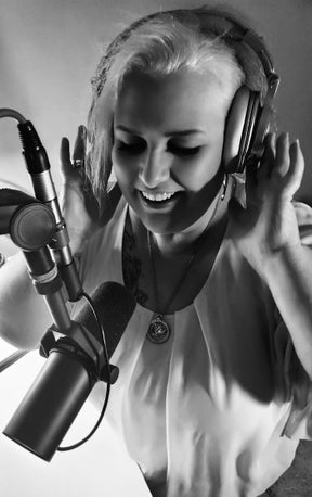 Regina Vera, Hypnose-Coachin, beim Einsprechen einer geführten Hypnose - freudig lächelnd mit Mikrofon und Kopfhörern in ihrem Studio.