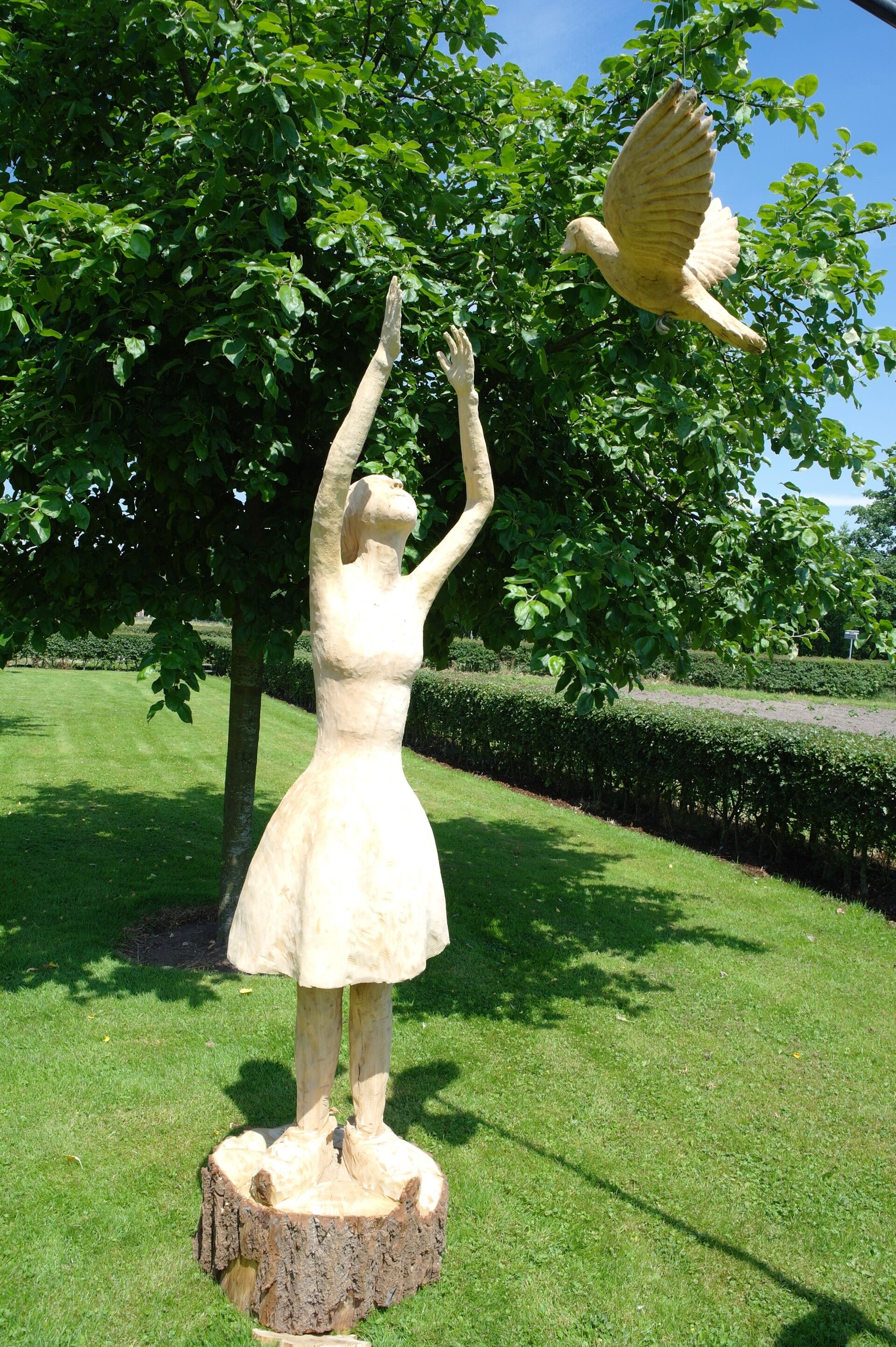 Houtsculptuur van een meisje die zich uitstrekt naar een vliegende duif