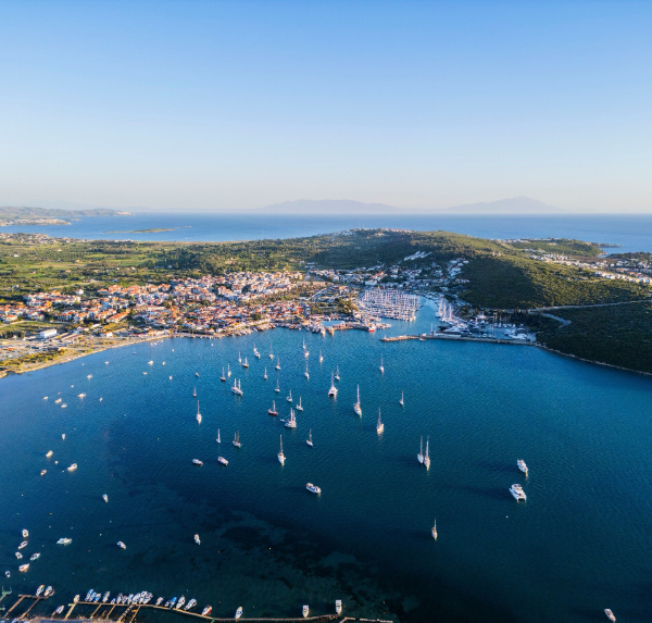 Luchtfoto van een grote beschutte baai met tientallen zeiljachten voor anker, een jachthaven en een kustplaats in Griekenland.