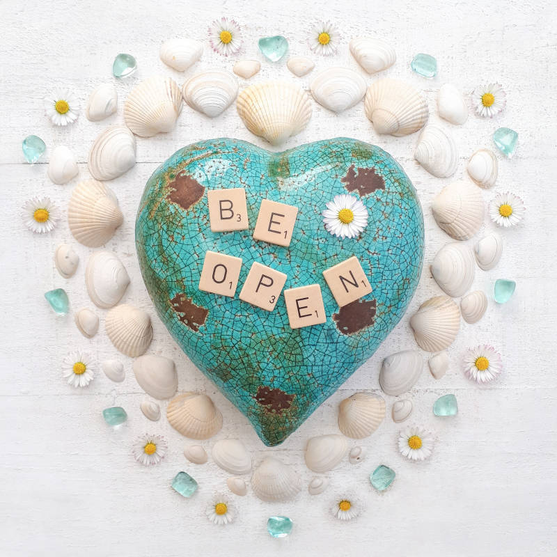 Wenskaart met een stenenhart waarop de letters be open liggen. Margrietjes, schelpen en obsidiaan.