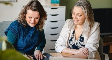 twee vrouwen die naar een tablet kijken en overleggen