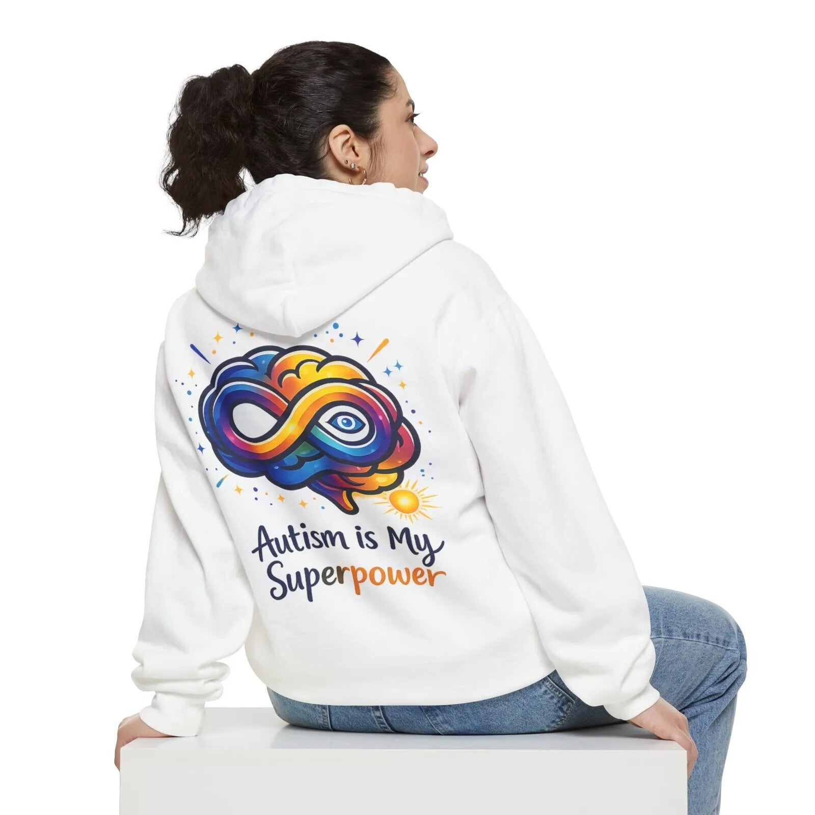Woman seated in a white hoodie featuring a colorful infinity symbol and the words “Autism Is My Superpower” across the back.