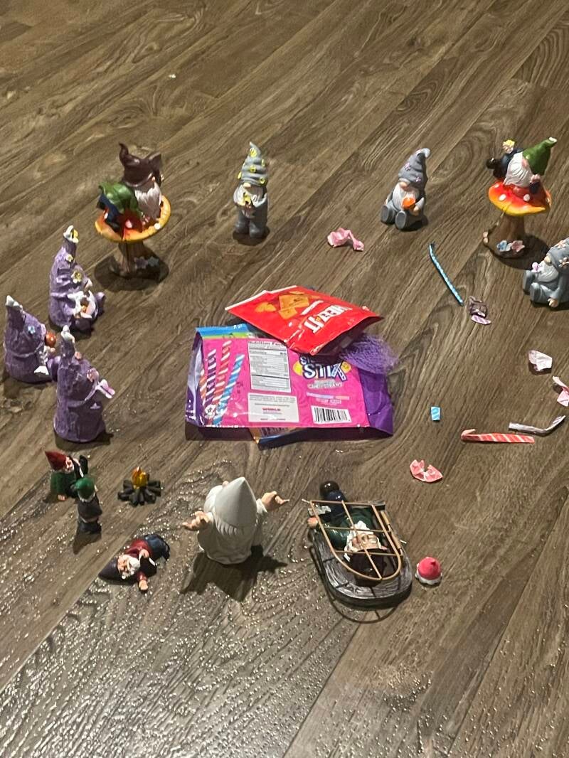 Several gnomes on the kitchen floor surrounding a pile of candy wrappers
