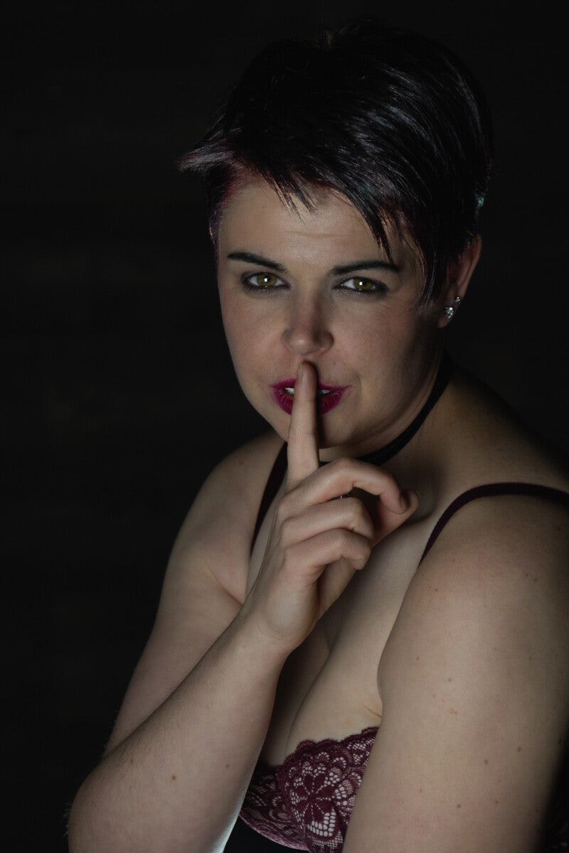 Low-key studio portret van een vrouw met kort donker haar die met haar vinger op haar lippen het shh-gebaar maakt, gefotografeerd door Timeless Takes.