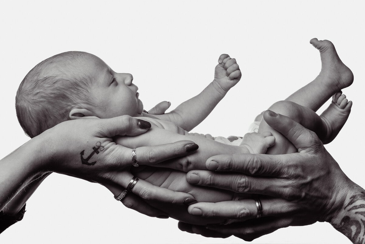 Spontane newborn en gezinsfotografie in zwart-wit van een baby in de handen van de ouders, portfoliobeeld van Timeless Tales.