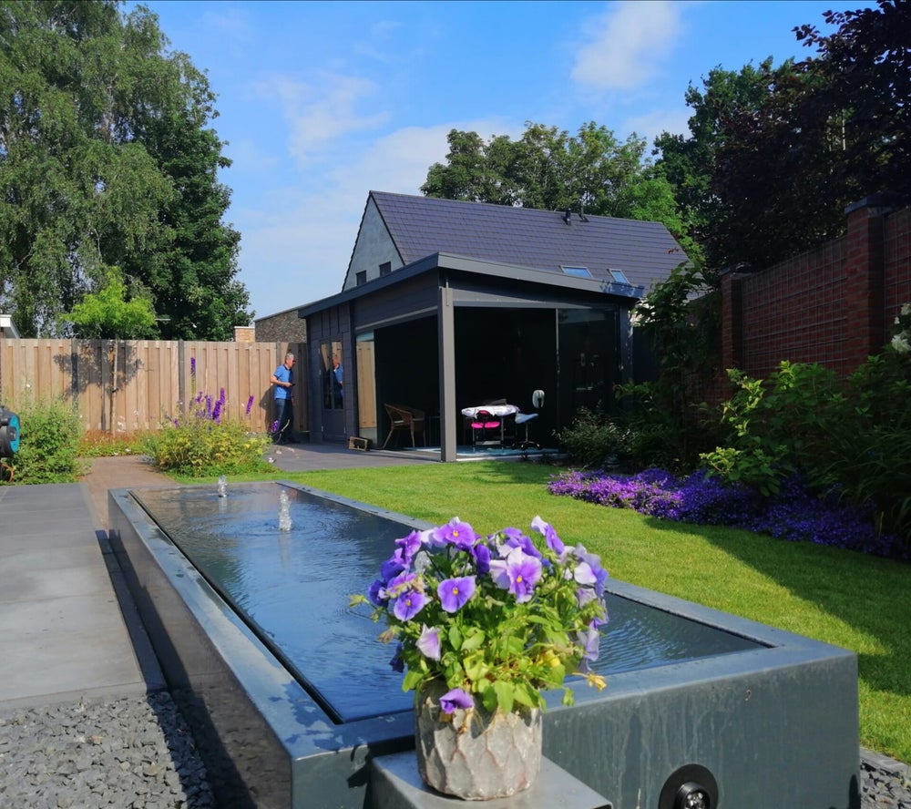 Overzicht van de praktijktuin met bloemen, waterornament en het bijgebouw