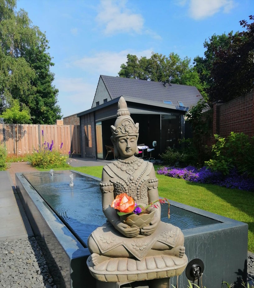 Een beeld met bloemen bij het waterornament in Nancy’s praktijktuin