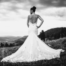 photos de mariée sur une colline, de dos, robe sirène, coiffure d'un chignon relevé mains sur les hanches, robe de mariée blanche, montagne et sapin dans le cadre
