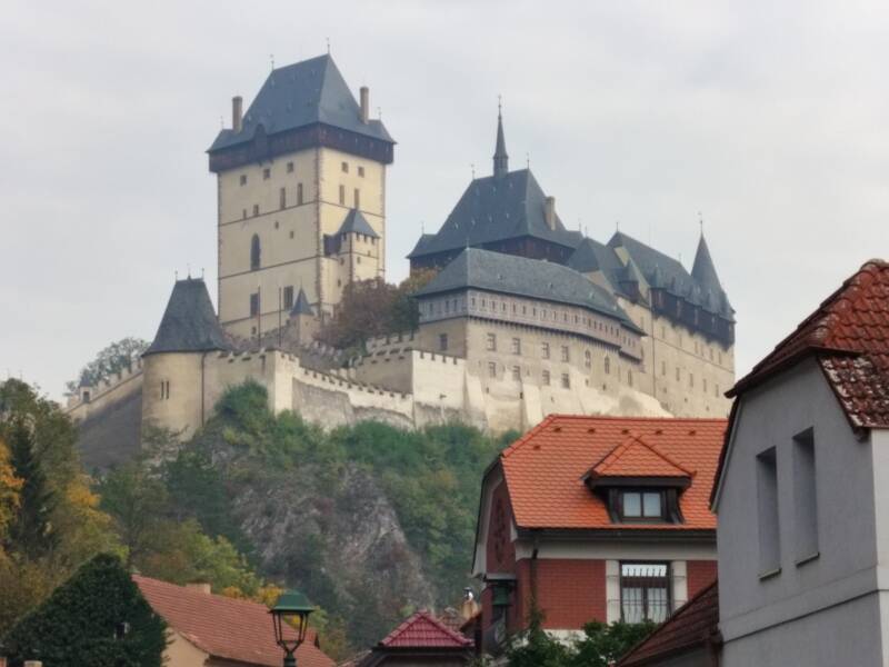 Dramatic view of Karlštejn Castle perched on a forested hilltop near Prague, showcasing its iconic Gothic towers and fortress walls.