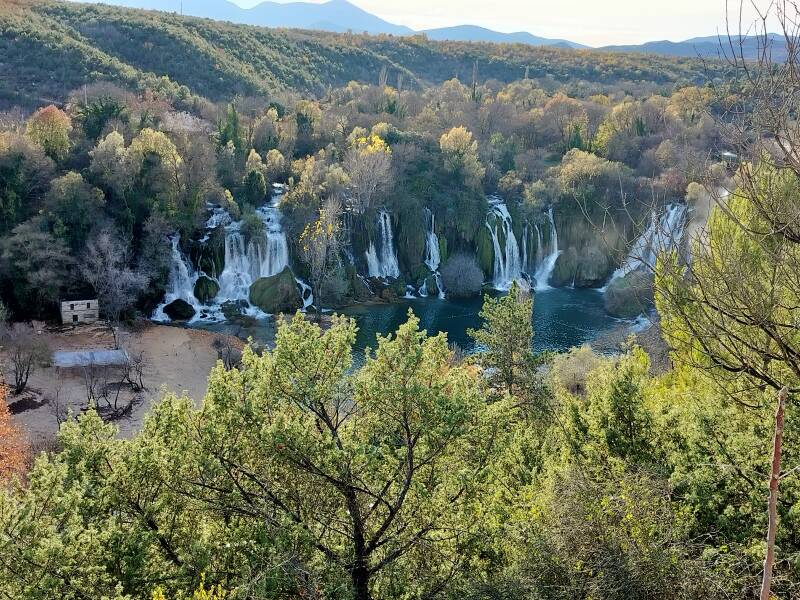 Panoramic view of Kravica Waterfalls cascading into emerald pools surrounded by forest.