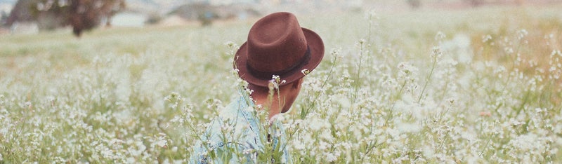 Ein Mann mit braunem Hut sitzt in einem Blumenfeld