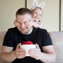 Enfant qui cache les yeux de son papa et lui offre un cadeau