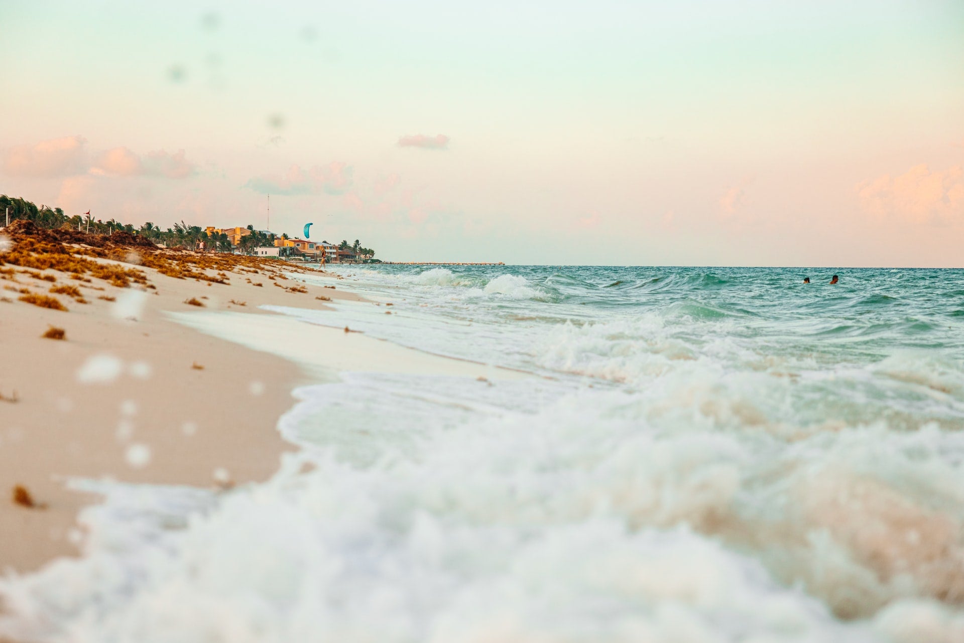Image of the Caribbean displaying the crystal clear ocean with foamy waves gently washing onto a pristine white sandy beach.