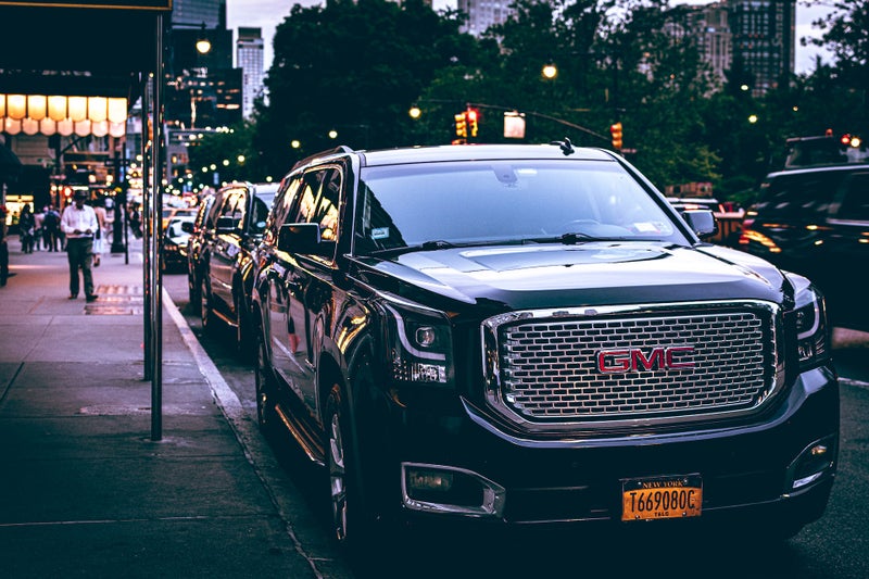 Luxury GMC SUV parked on a city street in the evening with urban lights and people in the background.