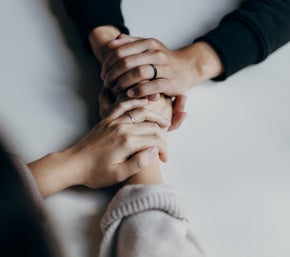 Two people sit at a table holding hands. One person is wearing a black ring. The background is blurred.