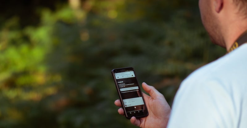 Man in een natuurlijke omgeving bekijkt een smartphone met een informatieve website op het scherm.